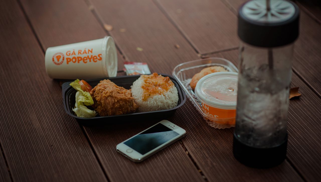A tasty Popeyes meal featuring fried chicken, rice, and a smartphone on a wooden table.